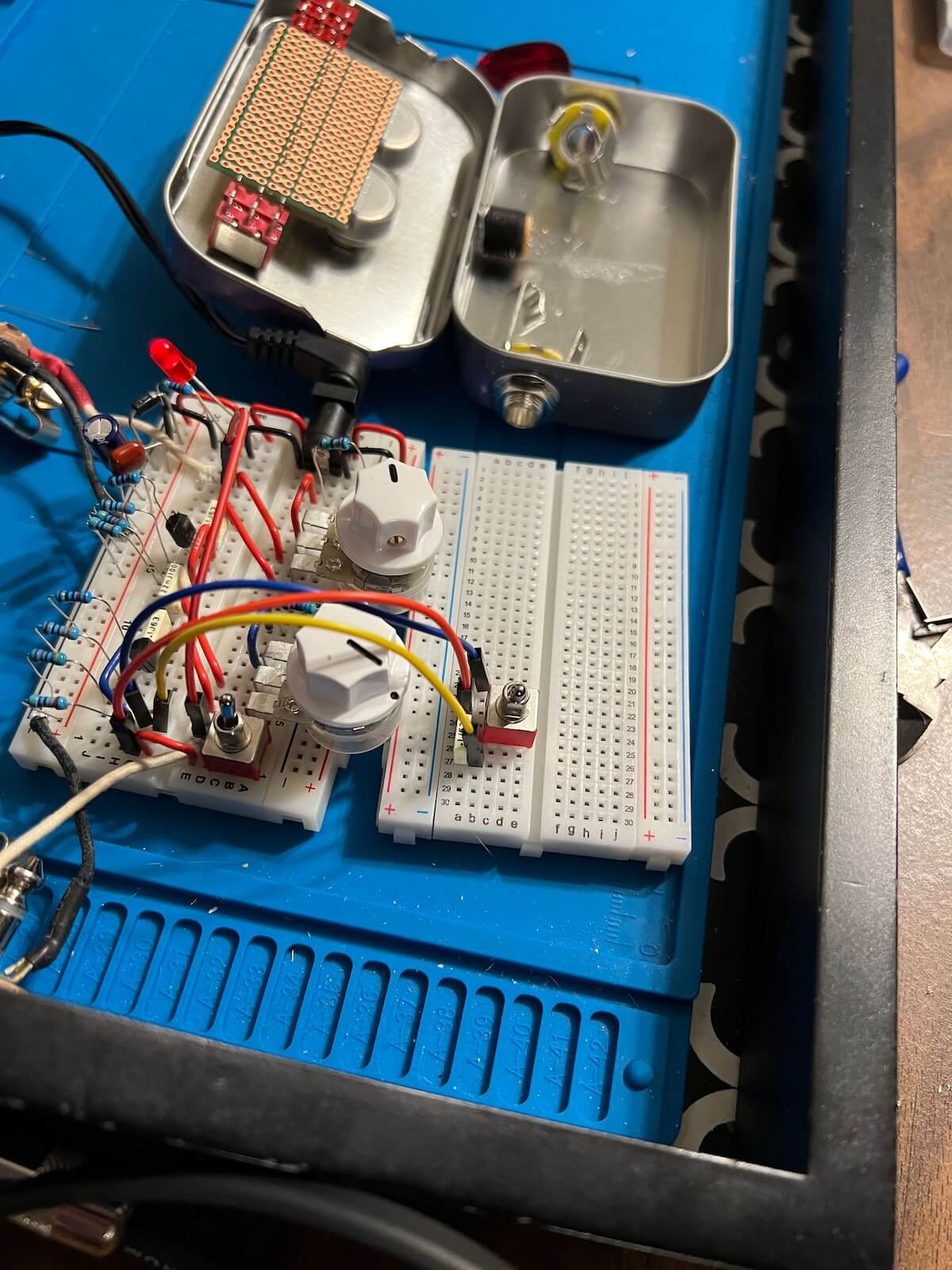 Breadboard prototype beside the open tin enclosure during circuit development