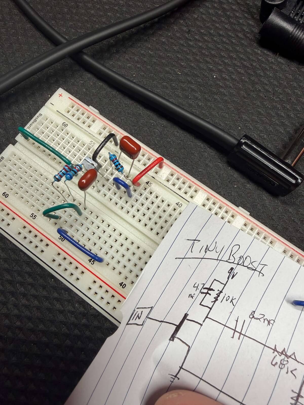 JFET boost circuit being developed on a breadboard beside a hand-drawn schematic